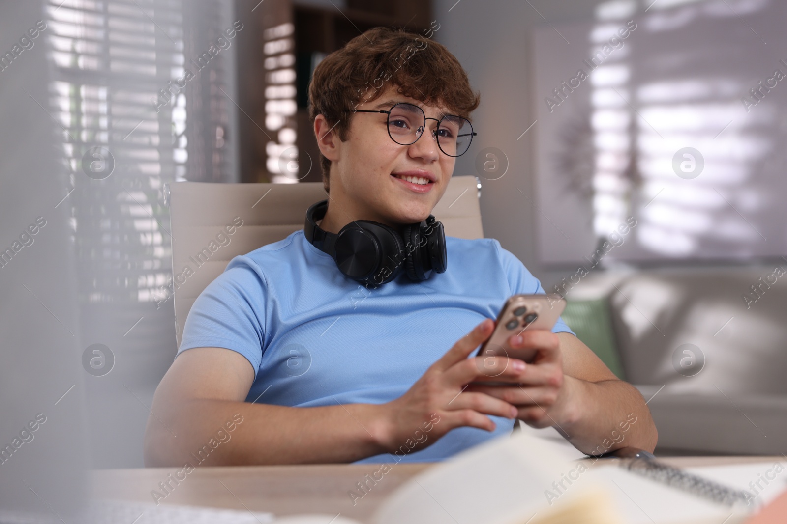 Teenage student with headphones using smartphone while studying at home Photo of Teenage student with headphones using smartphone while studying at home