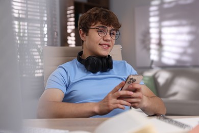 Photo of Teenage student with headphones using smartphone while studying at home