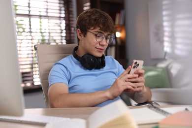 Photo of Teenage student with headphones using smartphone while studying at home