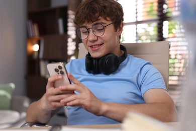 Photo of Teenage student with headphones using smartphone while studying at home