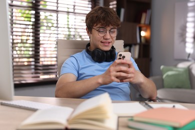 Photo of Teenage student with headphones using smartphone while studying at home
