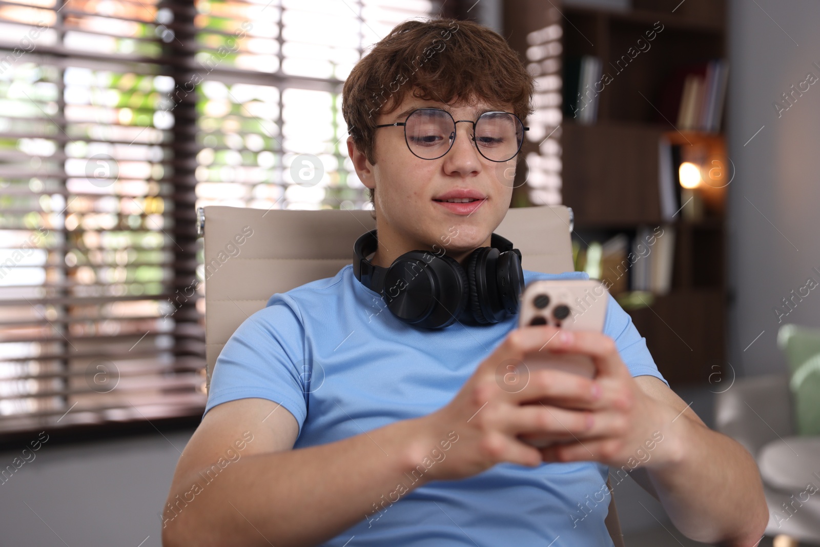 Teenage student with headphones using smartphone while studying at home Photo of Teenage student with headphones using smartphone while studying at home