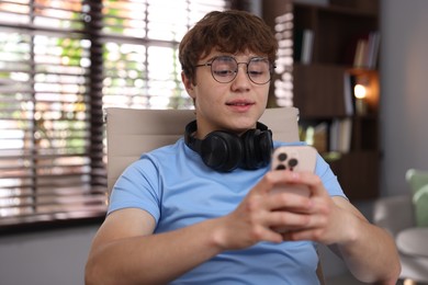Photo of Teenage student with headphones using smartphone while studying at home