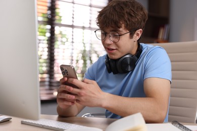 Photo of Teenage student with headphones using smartphone while studying at home