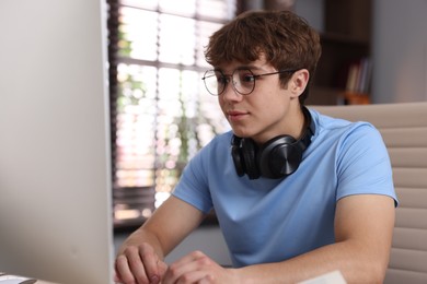 Photo of Teenage student with headphones using computer while studying at home