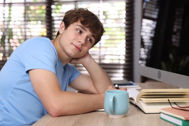 Photo of Teenage student taking notes while studying at table indoors
