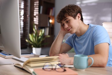Photo of Teenage student studying at table with books and computer indoors