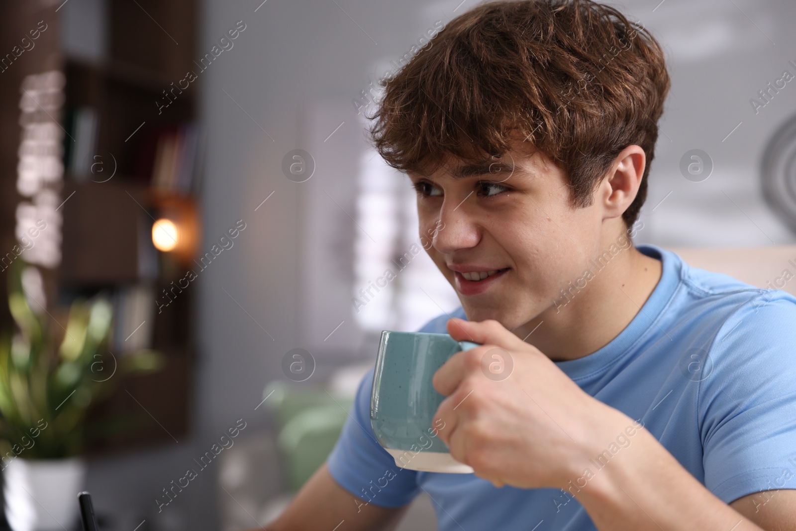 Teenage boy with cup of drink at home, space for text Photo of Teenage boy with cup of drink at home, space for text