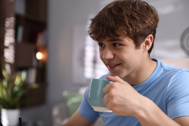 Photo of Teenage boy with cup of drink at home, space for text