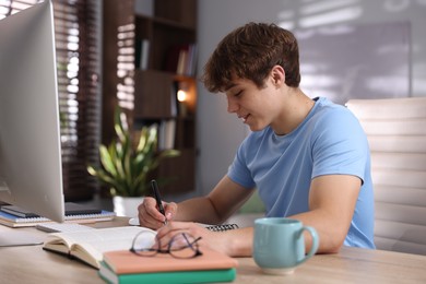Photo of Teenage student taking notes while studying at table indoors