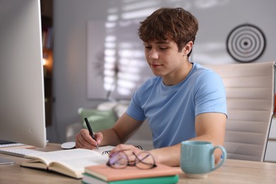 Photo of Teenage student taking notes while studying at table indoors