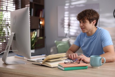 Photo of Teenage student using computer while studying at table indoors