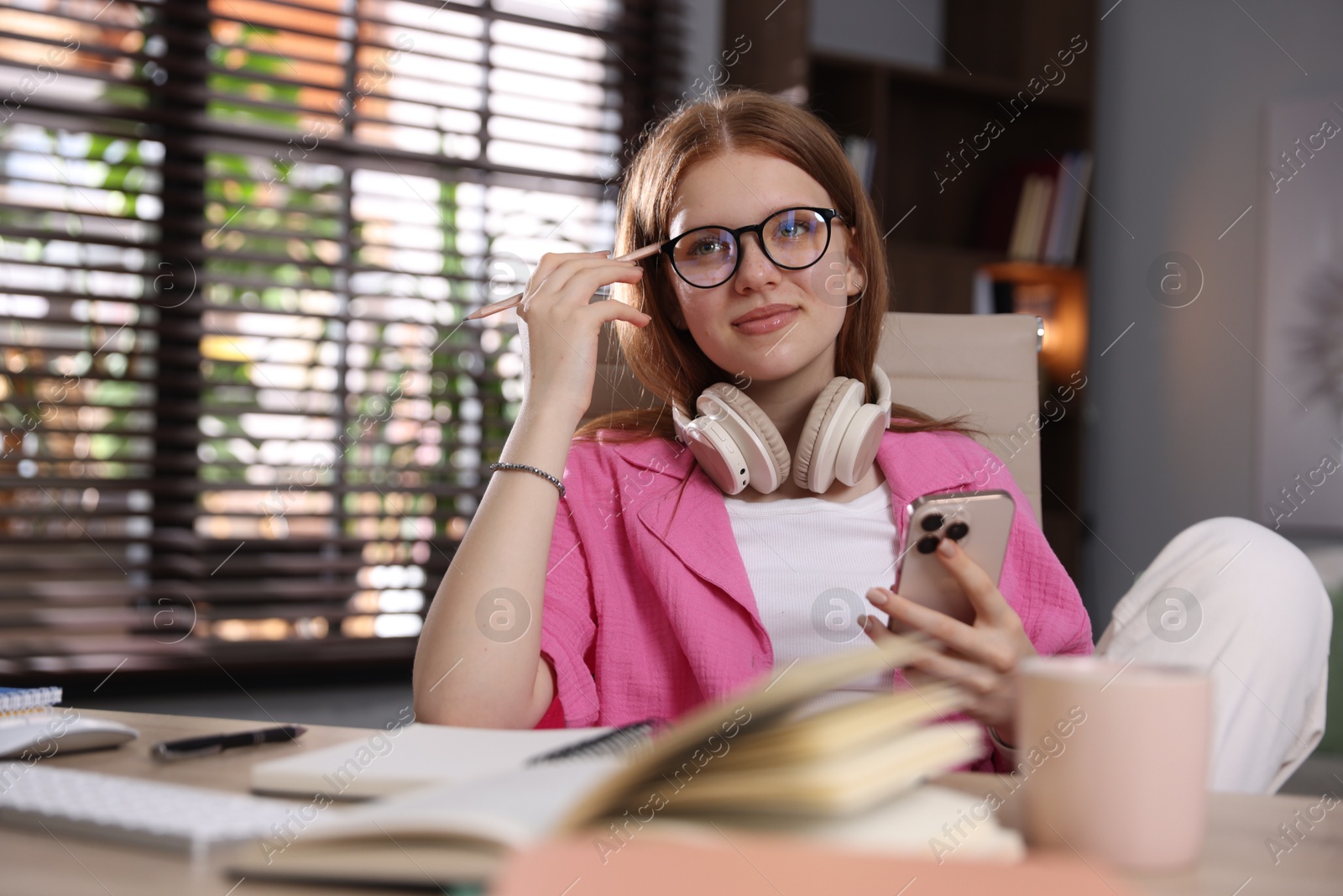 Teenage student with headphones using smartphone while studying at home Photo of Teenage student with headphones using smartphone while studying at home