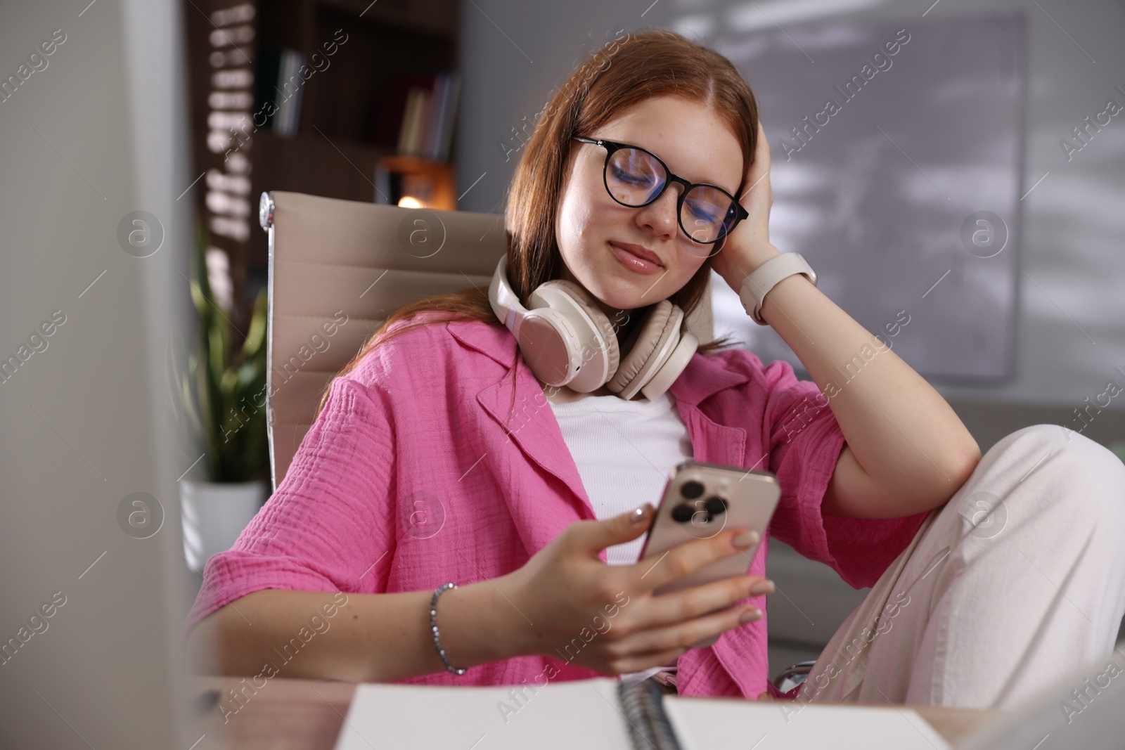 Teenage student with headphones using smartphone while studying at home Photo of Teenage student with headphones using smartphone while studying at home