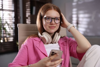Photo of Teenage student with headphones using smartphone while studying at home
