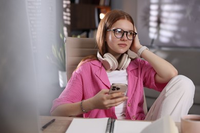 Photo of Teenage student with headphones using smartphone while studying at home