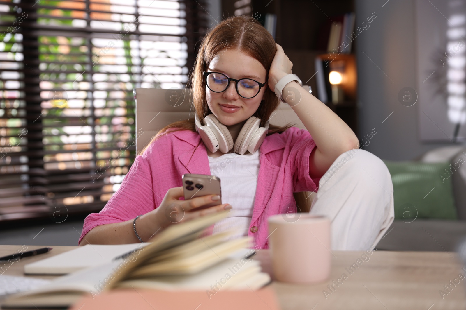 Teenage student with headphones using smartphone while studying at home Photo of Teenage student with headphones using smartphone while studying at home