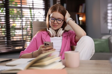 Photo of Teenage student with headphones using smartphone while studying at home
