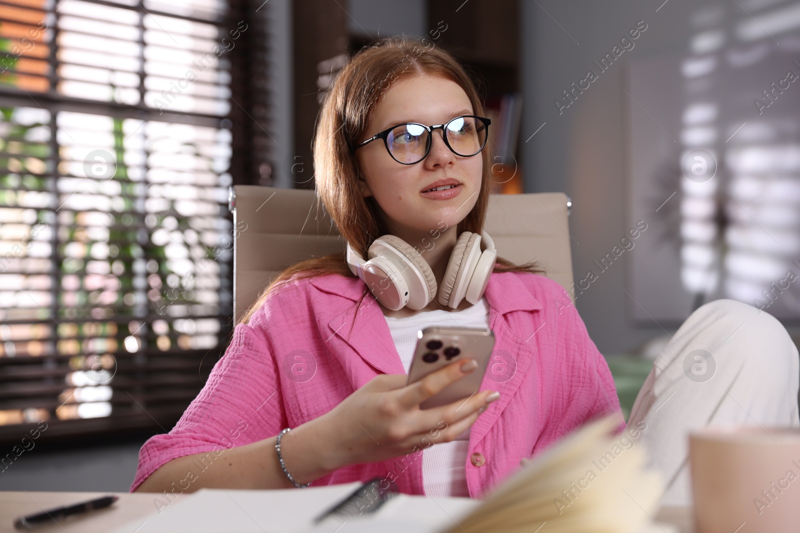Teenage student with headphones using smartphone while studying at home Photo of Teenage student with headphones using smartphone while studying at home