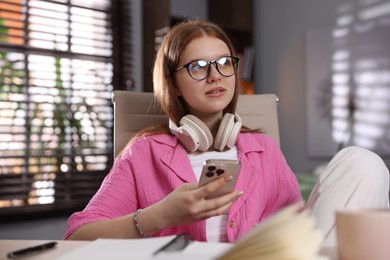Photo of Teenage student with headphones using smartphone while studying at home