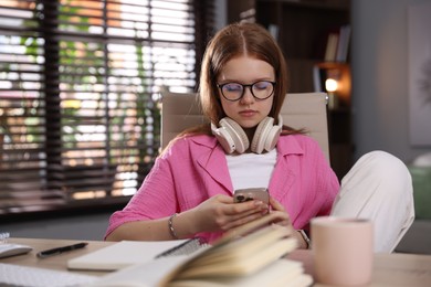 Photo of Teenage student with headphones using smartphone while studying at home