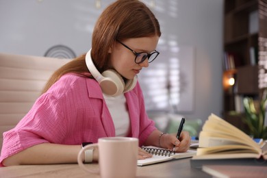Photo of Teenage student taking notes while studying at table indoors