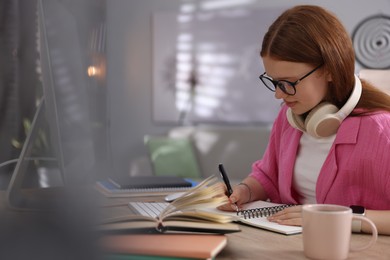 Photo of Teenage student taking notes while studying at table indoors