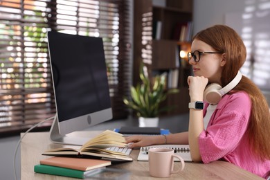 Photo of Teenage student with headphones using computer while studying at table indoors