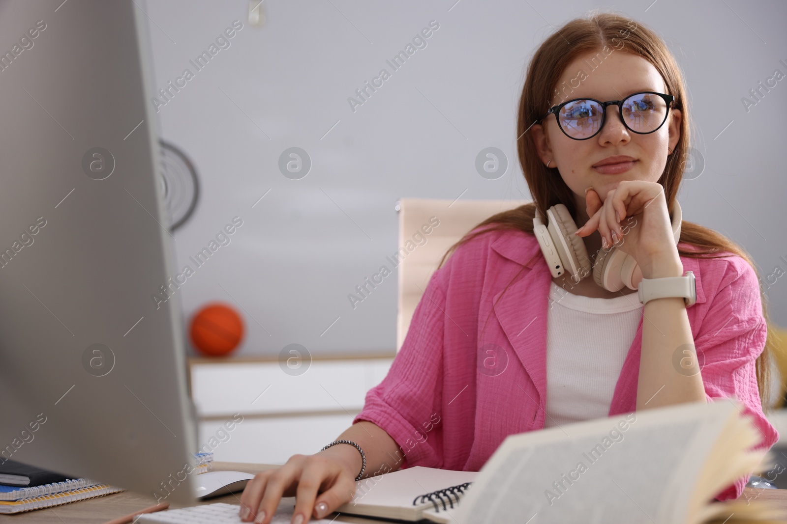 Teenage student with headphones using computer while studying at table indoors Photo of Teenage student with headphones using computer while studying at table indoors