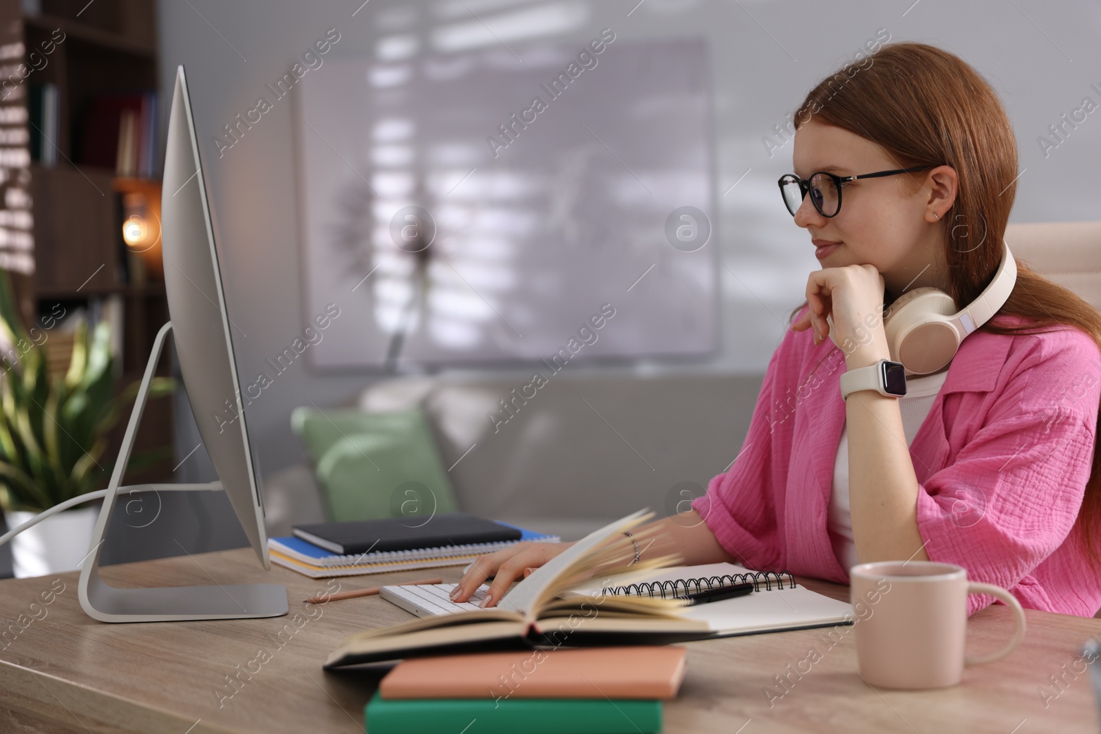Teenage student with headphones using computer while studying at table indoors Photo of Teenage student with headphones using computer while studying at table indoors