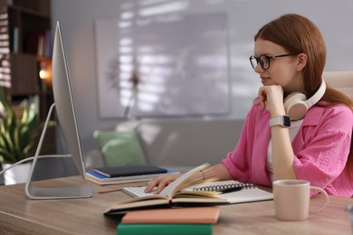 Photo of Teenage student with headphones using computer while studying at table indoors