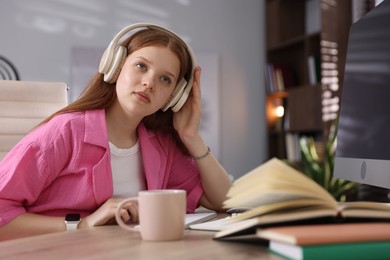 Photo of Teenage student in headphones studying at table indoors