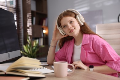 Photo of Teenage student in headphones studying at table indoors