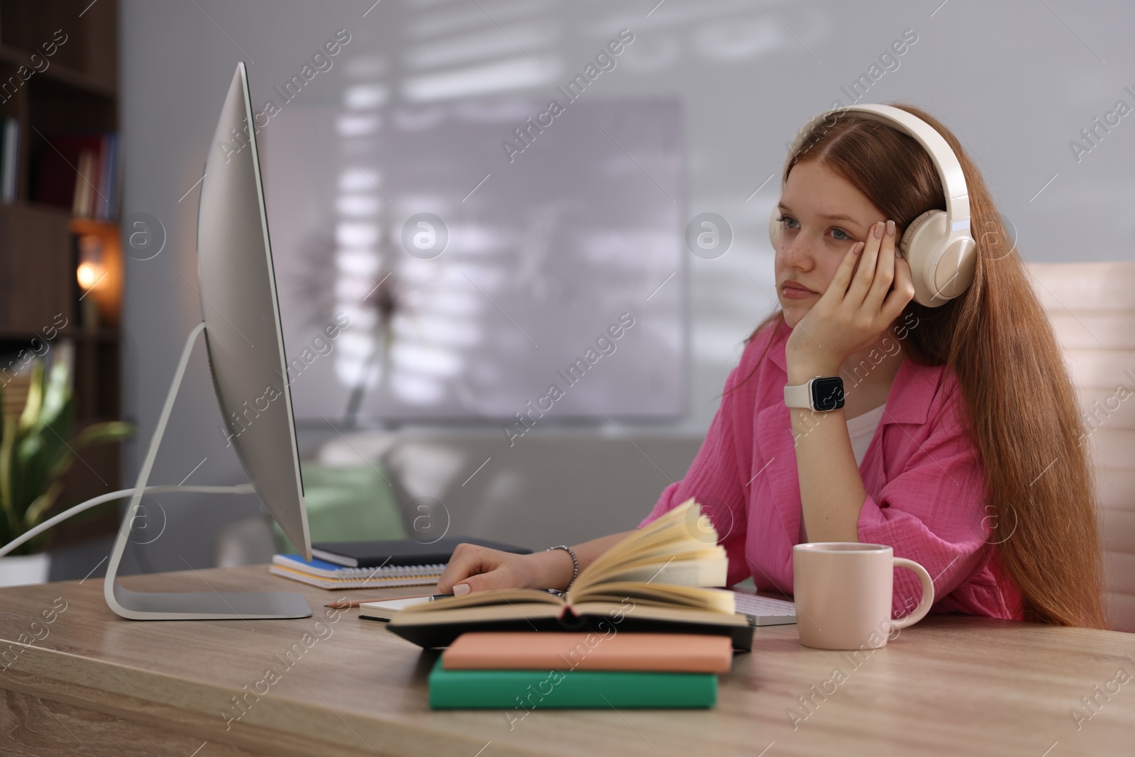 Teenage student in headphones studying at table indoors Photo of Teenage student in headphones studying at table indoors