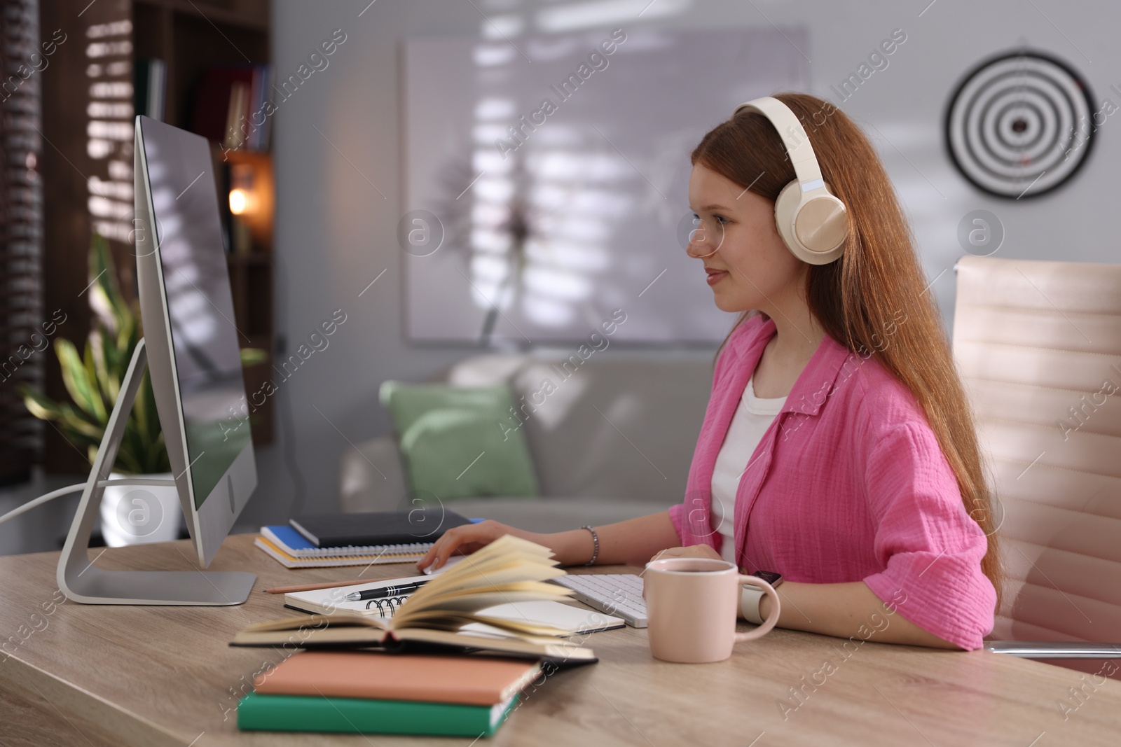 Teenage student with headphones using computer while studying at table indoors Photo of Teenage student with headphones using computer while studying at table indoors