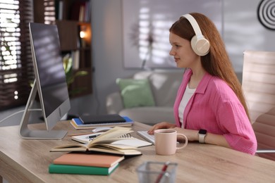 Photo of Teenage student with headphones using computer while studying at table indoors
