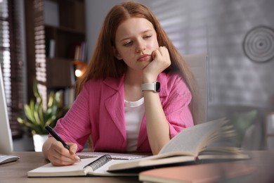 Photo of Teenage student taking notes while studying at table indoors
