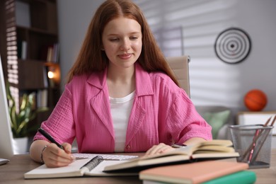 Photo of Teenage student taking notes while studying at table indoors