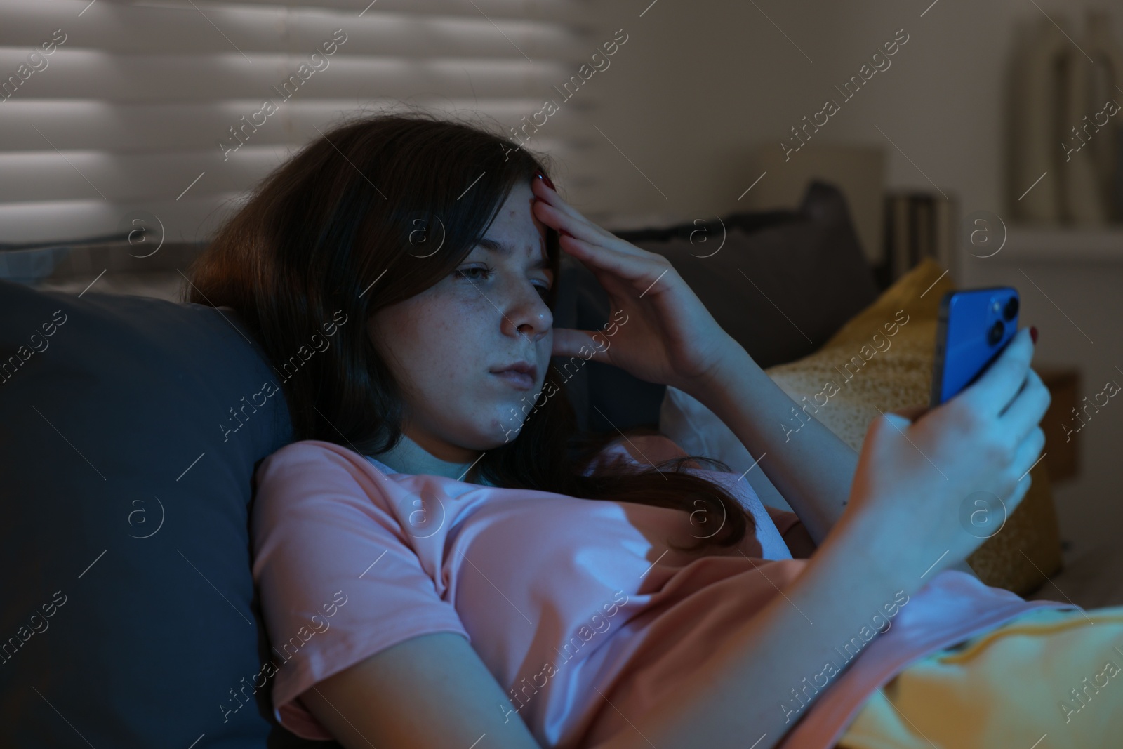 Upset teenage girl with smartphone on bed at night Photo of Upset teenage girl with smartphone on bed at night