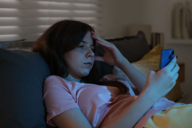 Photo of Upset teenage girl with smartphone on bed at night