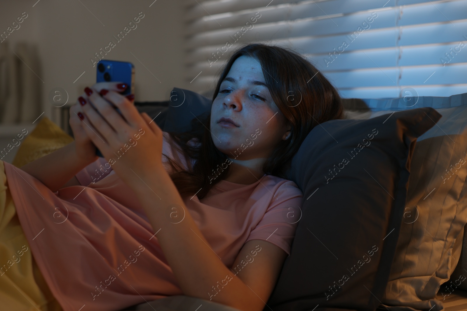 Photo of Upset teenage girl with smartphone on bed at night