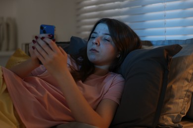 Photo of Upset teenage girl with smartphone on bed at night