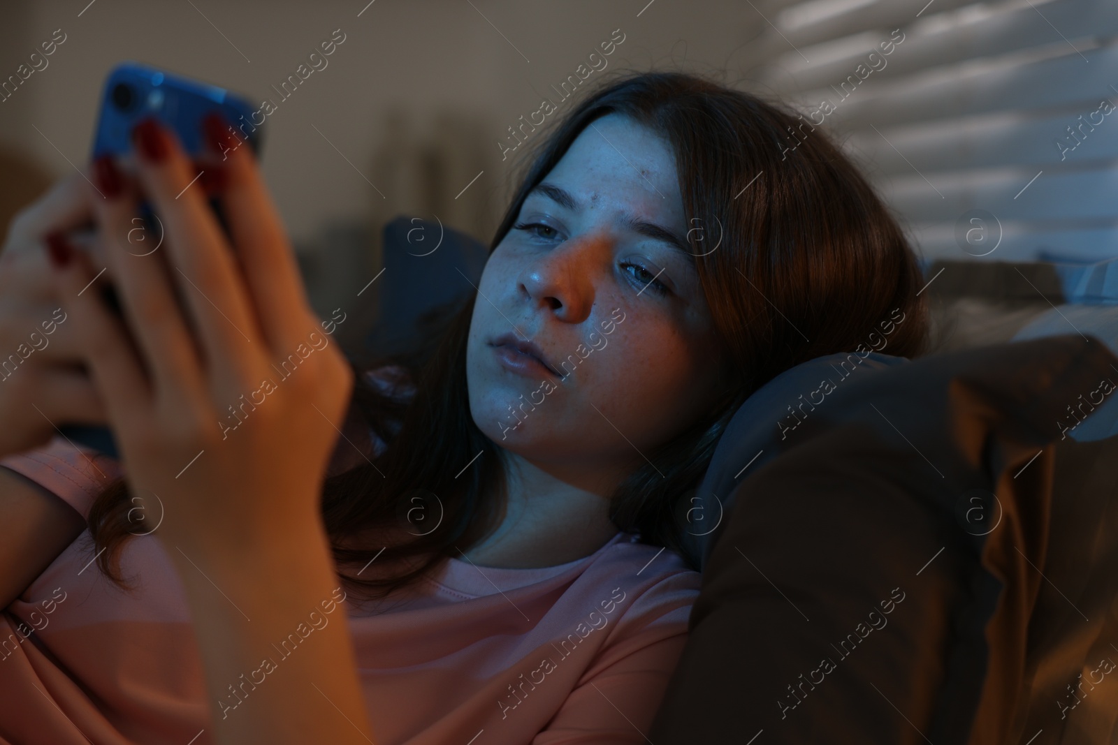 Upset teenage girl with smartphone on bed at night Photo of Upset teenage girl with smartphone on bed at night