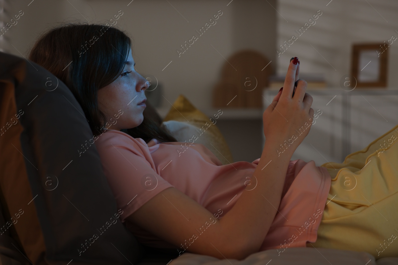 Upset teenage girl with smartphone on bed at night Photo of Upset teenage girl with smartphone on bed at night