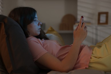 Photo of Upset teenage girl with smartphone on bed at night
