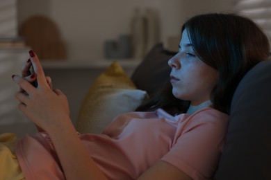 Photo of Upset teenage girl with smartphone on bed at night