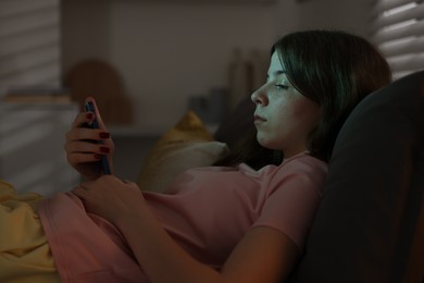 Photo of Upset teenage girl with smartphone on bed at night