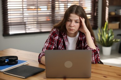 Photo of Stressed teenage girl studying at desk indoors