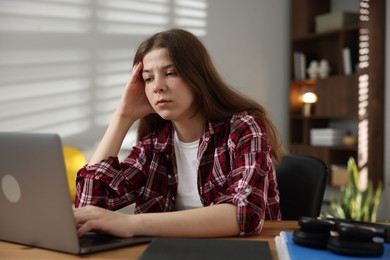 Photo of Stressed teenage girl studying at desk indoors