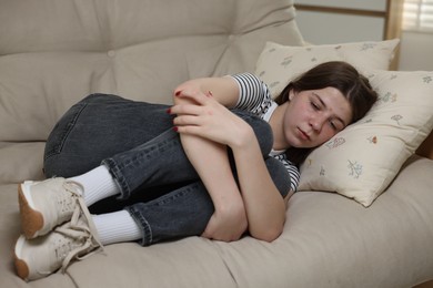 Photo of Depressed teenage girl lying on sofa at home